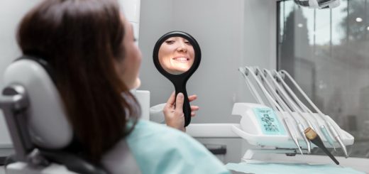 Patient in a dental chair holds a handheld mirror and smiles at her reflection during a checkup, with dental tools on a tray nearby.
