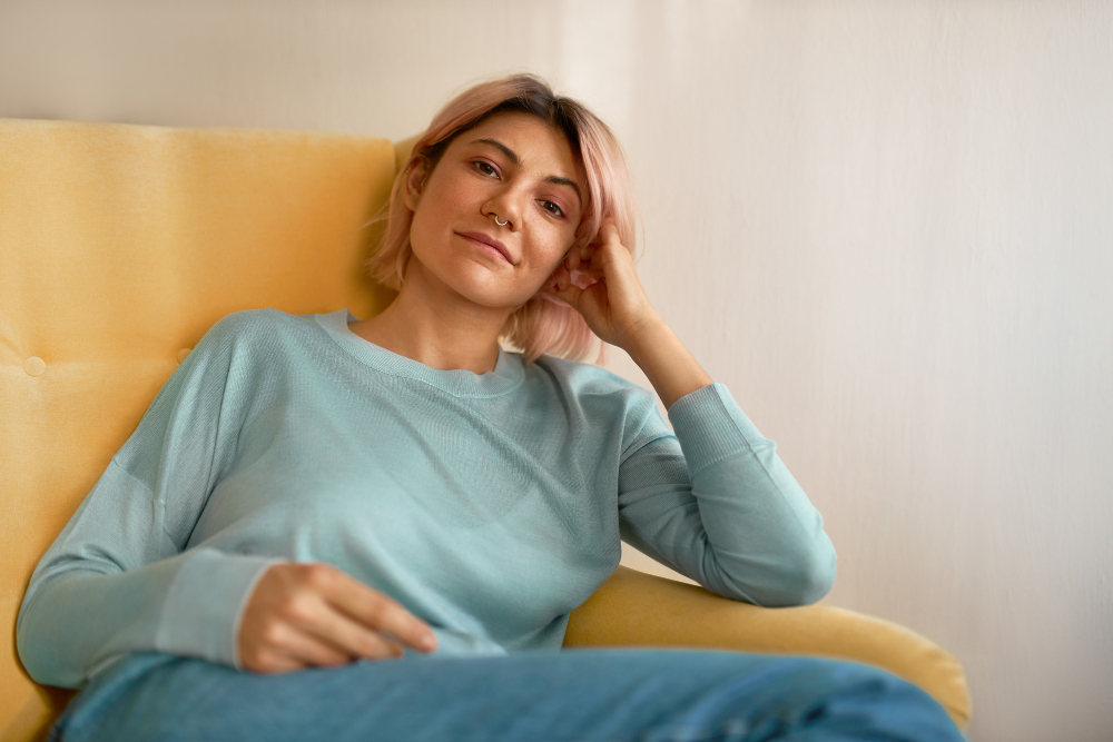 772266 - María Santianes Salud Hormonal | SoloSalud.net Calm, casual portrait of a person lounging on a mustard-yellow chair in a light blue sweater.
