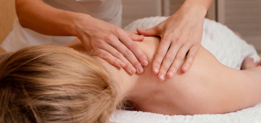 Therapist massaging a person’s upper back while they lie face down on a spa table.