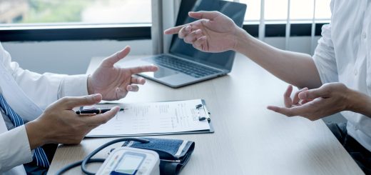 Two professionals review medical forms on a desk, with a blood pressure monitor and laptop visible.
