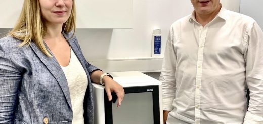 Two professionals pose beside a white medical analyzer with a touchscreen in a clean lab setting.