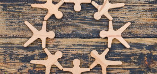 Eight wooden figure cutouts form a circle on a dark, weathered wooden surface, like people holding hands around a circle.