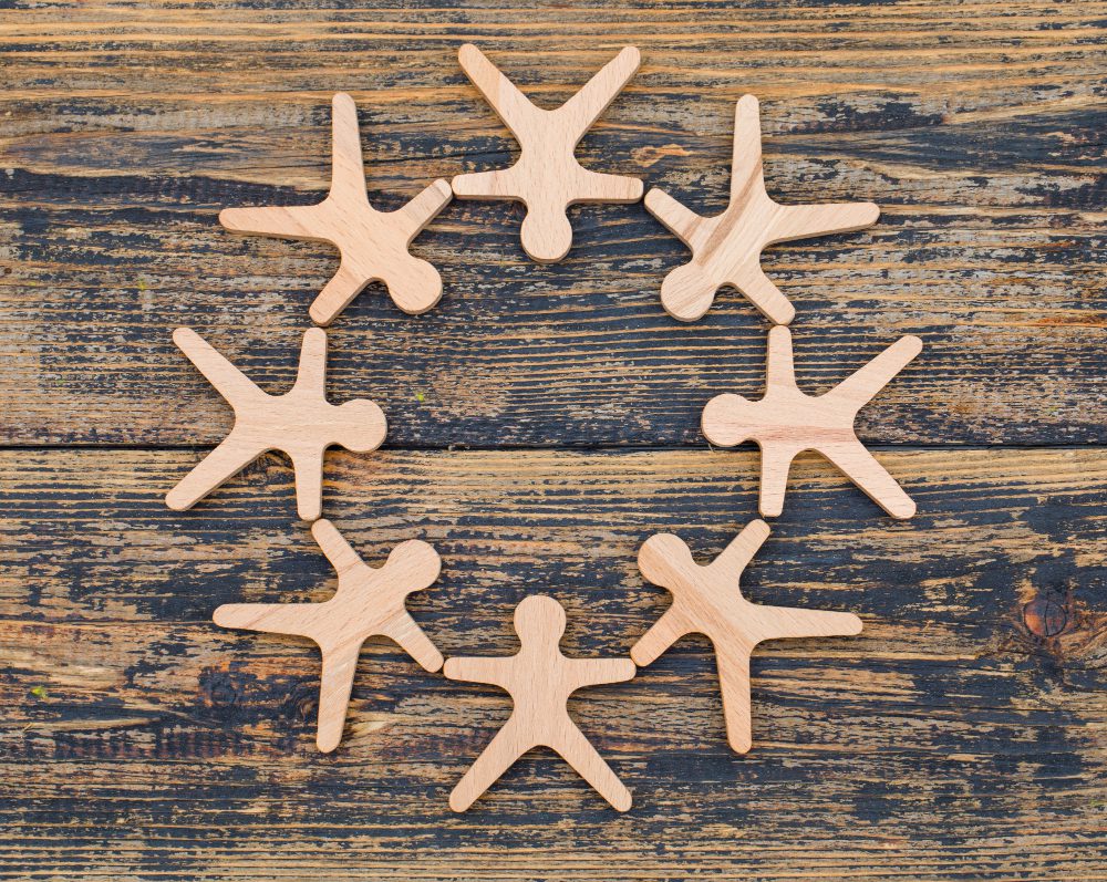 777564 - Institut Integratiu | SoloSalud.net Eight wooden figure cutouts form a circle on a dark, weathered wooden surface, like people holding hands around a circle.
