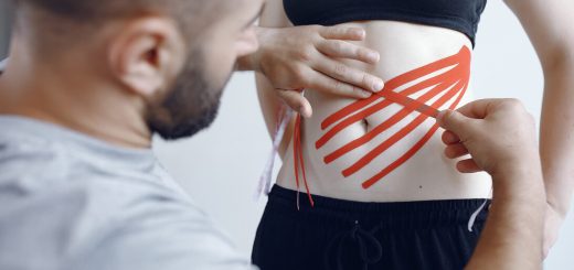 Therapist applies red kinesiology tape to a woman's lower abdomen for support or therapy.