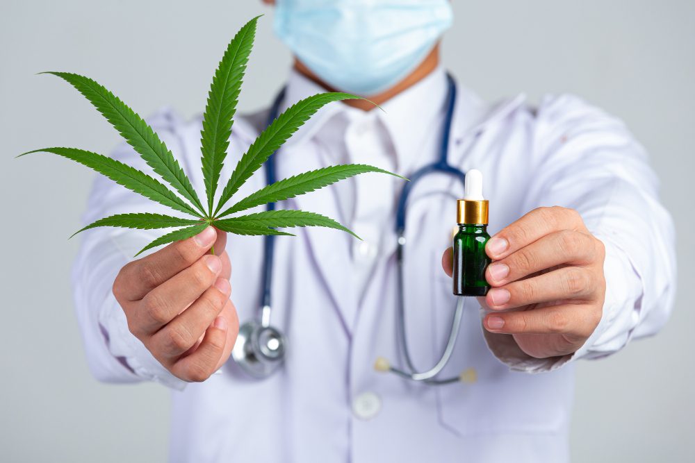 El uso medicinal del cannabis avanza con nuevas opciones terapéuticas - Healthcare professional holding a cannabis leaf and a CBD oil dropper, illustrating medical cannabis treatment in a clinical setting