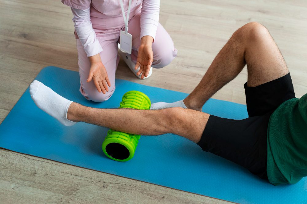 Therapist guiding leg foam rolling during a physical therapy session on a blue mat.