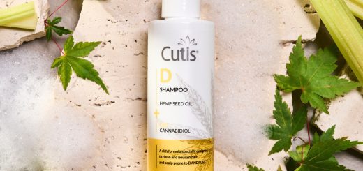 Cutis D Shampoo bottle with hemp seed oil and cannabidiol on a textured surface with green leaves around it (informational product shot)