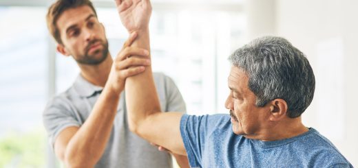 Therapist guiding a senior man through an elbow stretch in a bright clinic.