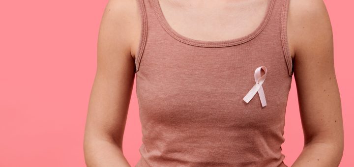 Person wearing a pink tank top with a pink breast cancer awareness ribbon pinned to the chest against a pink background for awareness.
