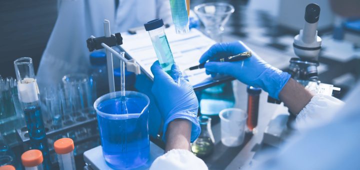 Lab technicians in blue gloves transfer blue liquid between test tubes with a pipette in a clinical lab vessel setup