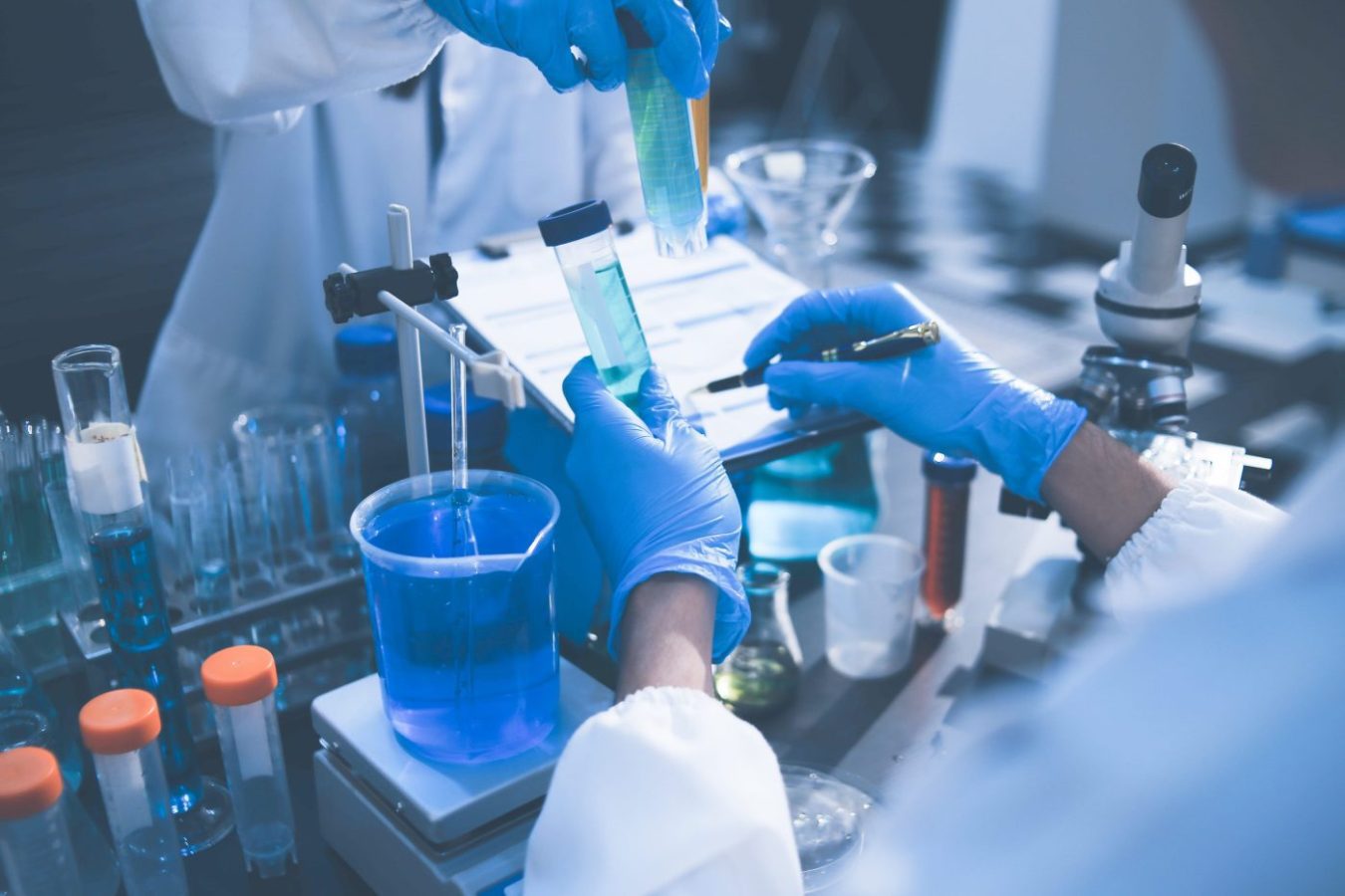 Researchers working in the clinical laboratory | SoloSalud.net Lab technicians in blue gloves transfer blue liquid between test tubes with a pipette in a clinical lab vessel setup